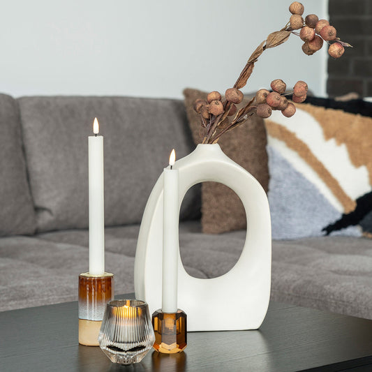 Moderne kamer met witte kaarsen in kandelaar, abstracte vaas met takken en stijlvolle kussens op grijze bank.