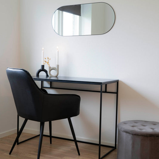 Minimalistisch bureau met zwarte stoel, spiegel en moderne kandelaars met brandende kaarsen op houten vloer.