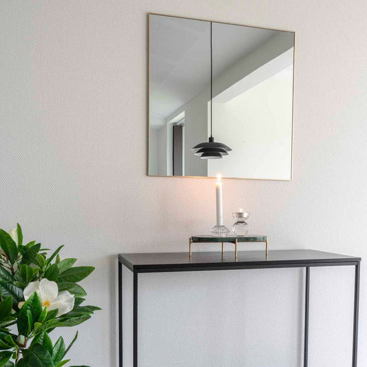 Console met spiegel en brandende kaars, hanglamp reflecterend in de spiegel, naast een groene plant.