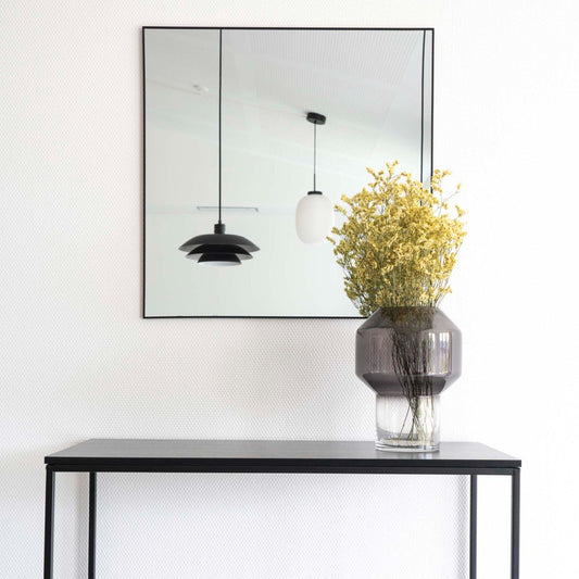 Zwart metalen tafel met vaas vol gele bloemen, spiegel reflecteert moderne hanglampen in minimalistisch interieur.