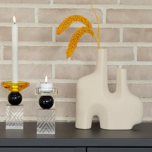 Moderne witte kandelaars en beige vaas met gele gedroogde bloemen tegen een bakstenen muur.