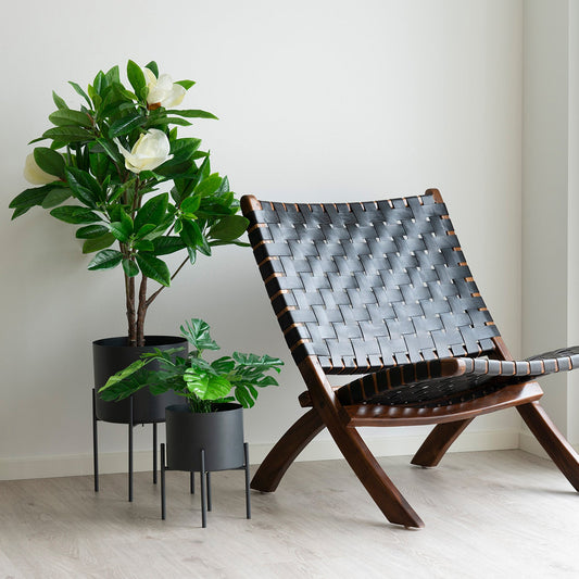 Donker houten stoel met gevlochten zitting naast groene kamerplanten in zwarte potten op lichte houten vloer.