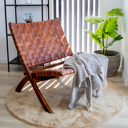 Modern houten stoel met gevlochten leren zitting, grijze deken, naast groene plant op ronde mat in lichte kamer.