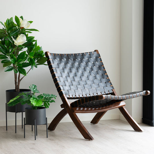 Donkerbruine houten stoel met zwart gevlochten zitting naast groene planten in zwarte potten op houten vloer.