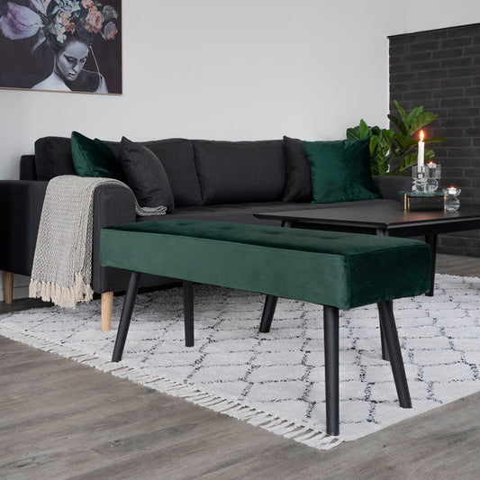 Moderne woonkamer met een donkergroene fluwelen bank, zwarte bank, kunst aan de muur en kaars op tafel.