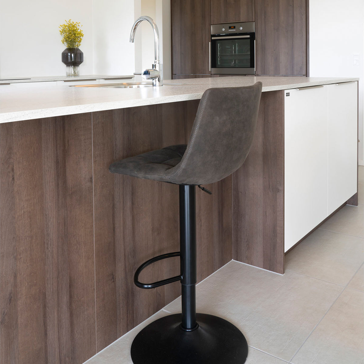 Moderne keuken met houten kasten, beige aanrecht, grijze barkruk en zwarte oven, strakke en sfeervolle inrichting.