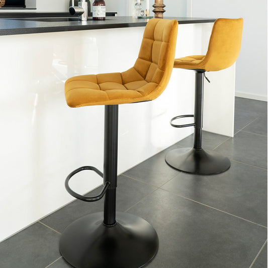 Mosterdgele barstoelen met zwarte metalen voet, geplaatst aan een moderne witte bar in een strakke ruimte.