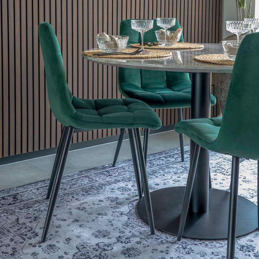 Donkergroen fluwelen eetkamerstoelen rond een marmeren tafel met glazen, op een Oosters tapijt.