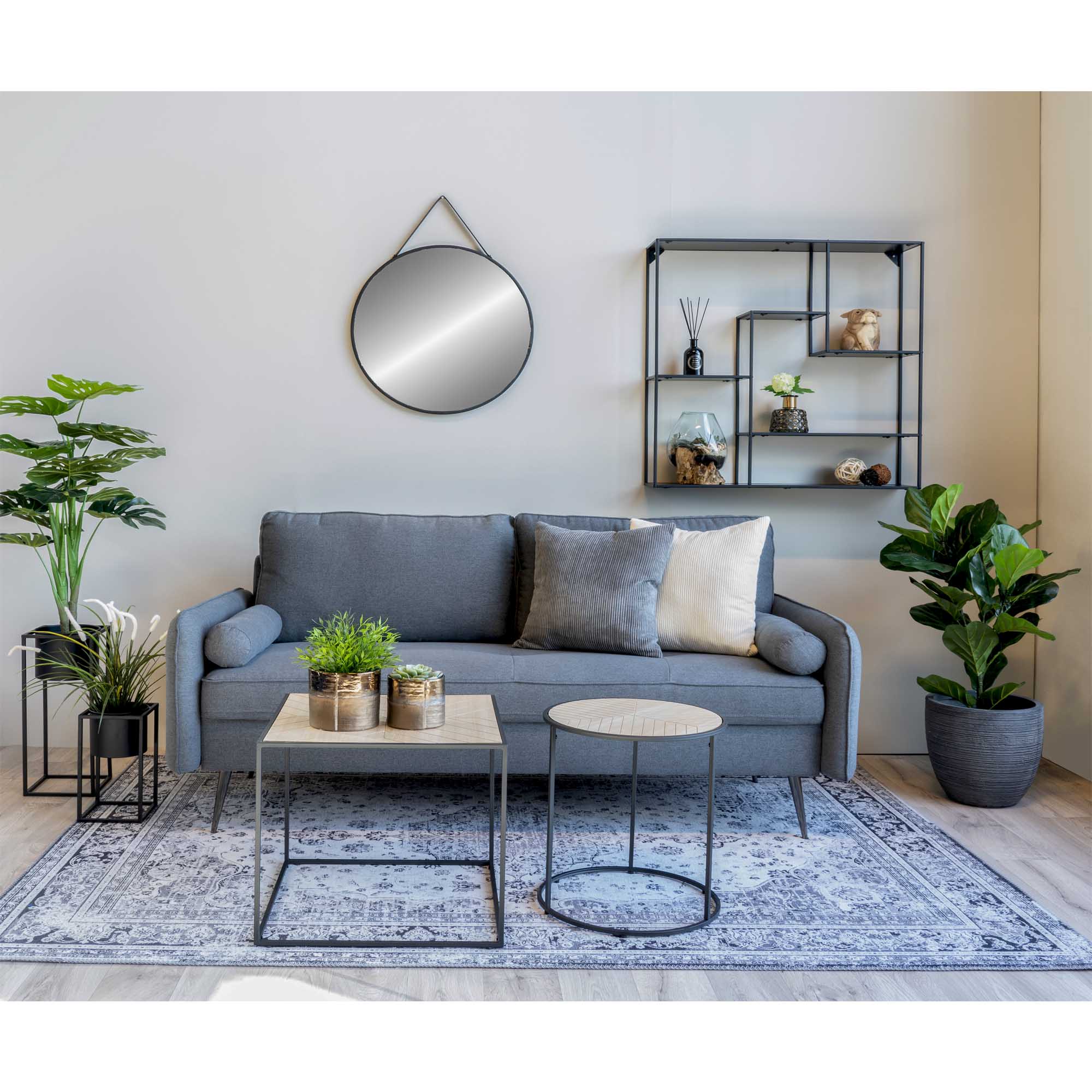Stijlvolle woonkamer met grijze bank, ronde spiegel, planten en decoratieve wandplanken op een sierlijk tapijt.