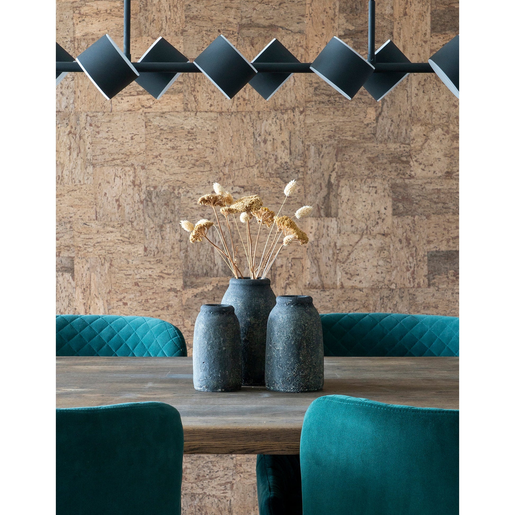 Donkergroene fluwelen stoelen rondom houten tafel met drie aardewerken vazen en gedroogde bloemen onder zwarte lamp.