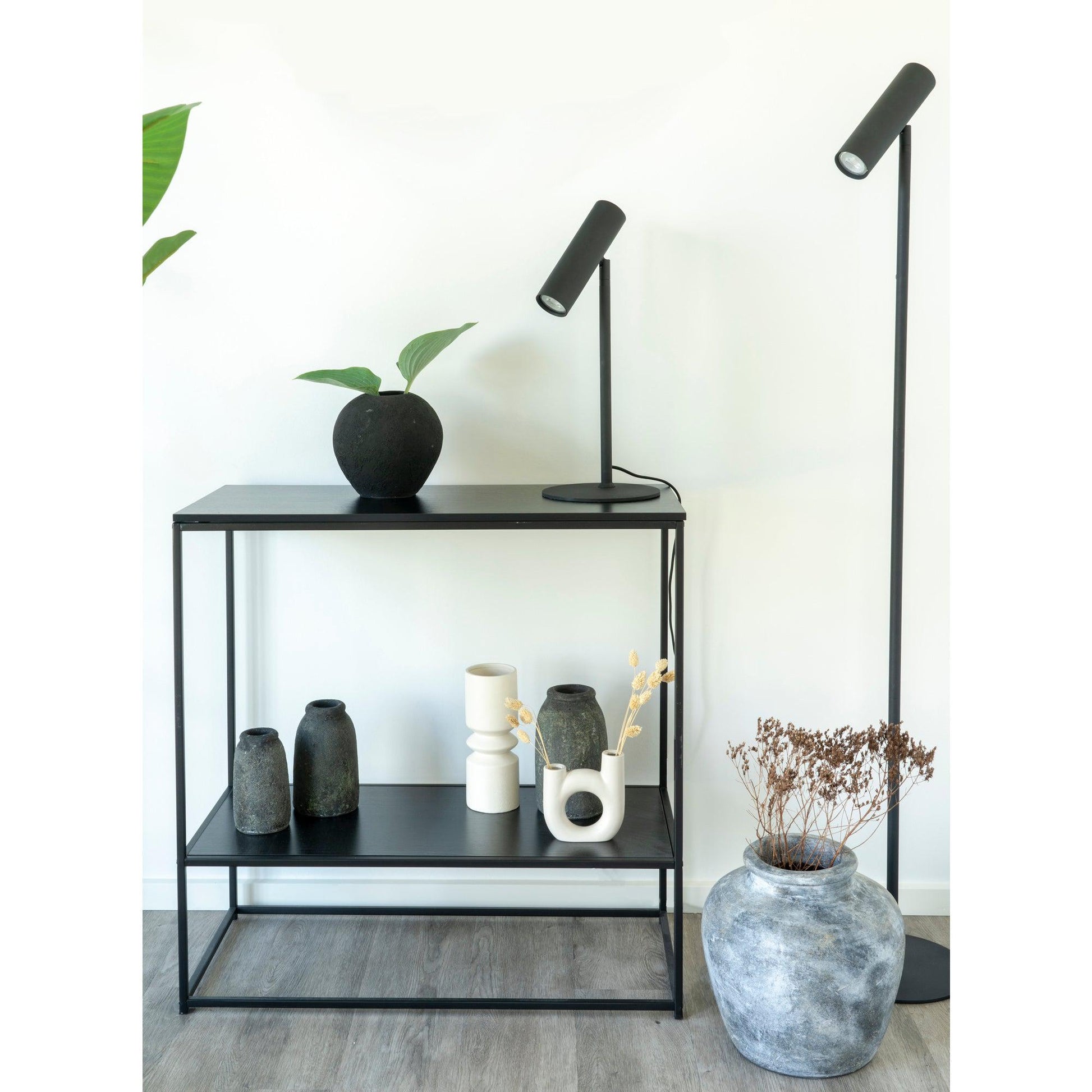 Zwarte metalen tafel met vazen en plant, minimalistische lampen ernaast, modern interieurontwerp.