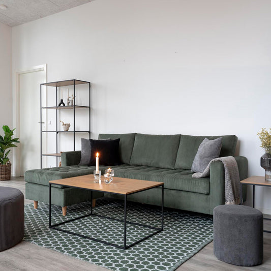 Stijlvolle woonkamer met groene bank, houten salontafel, brandende kaars en moderne decoraties op een patroonkleed.