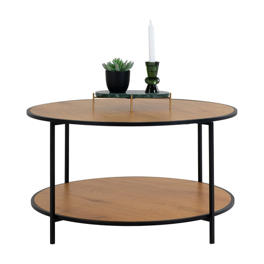 Ronde houten bijzettafel met zwarte metalen poten, versierd met een plant, boeken en een groene kandelaar.