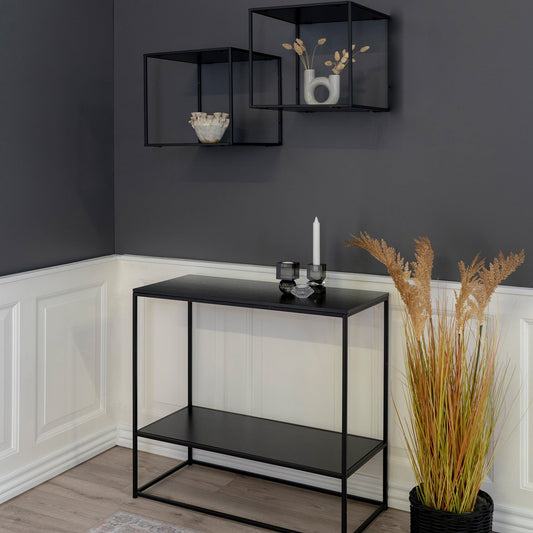 Moderne hoek met zwarte tafel, decoratieve kaarsen, glazen doosjes en droogbloemen op grijze muur.