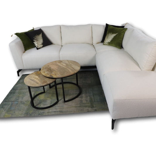 Luxe witte hoekbank met groene kussens en metalen salontafels op een blauwgroen tapijt.