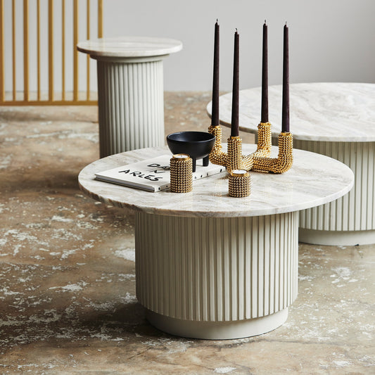 Marmeren salontafel met geribbelde basis, versierd met gouden kandelaars en een boek met opdruk "DIVINE ARLES".