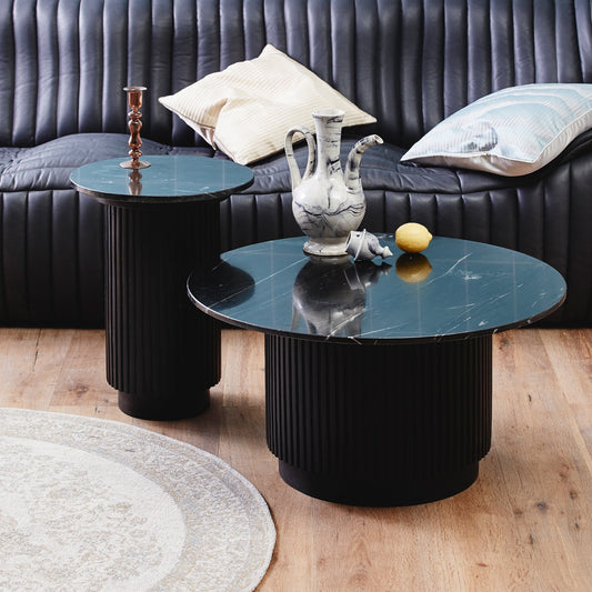 Zwarte marmeren salontafels met een vaas, kaars en citroen, voor een zwartleren bank met kussens.