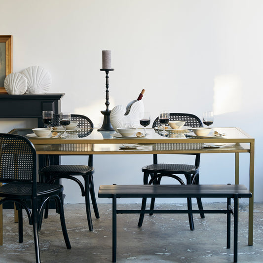 Stijlvolle eetkamer met zwarte stoelen rond een gouden tafel gedekt met rode wijn en witte schotels.