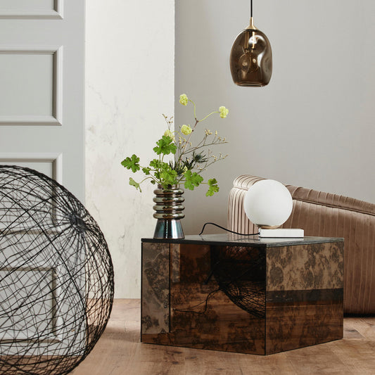 Stijlvolle woonkamer met moderne zilveren vaas, groene bloemen, zwarte hanglamp en luxe beige bank.