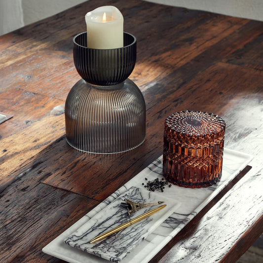 Glazen kaarsenhouder en decoratieve karaf op houten tafel, met marmeren plateau, gouden pen en Eiffeltoren-souvenir.