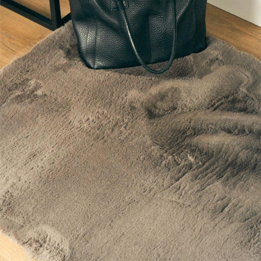 Grijs, pluizig vloerkleed met een zwart, leren tas erop, gelegen op een houten vloer in een kamer.