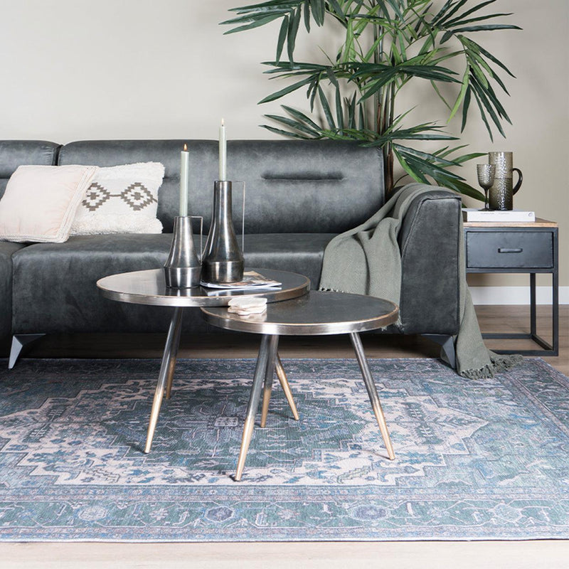Grijze bank met kussens, salontafel met kandelaars, groen plaid, plant en blauw patroon vloerkleed.