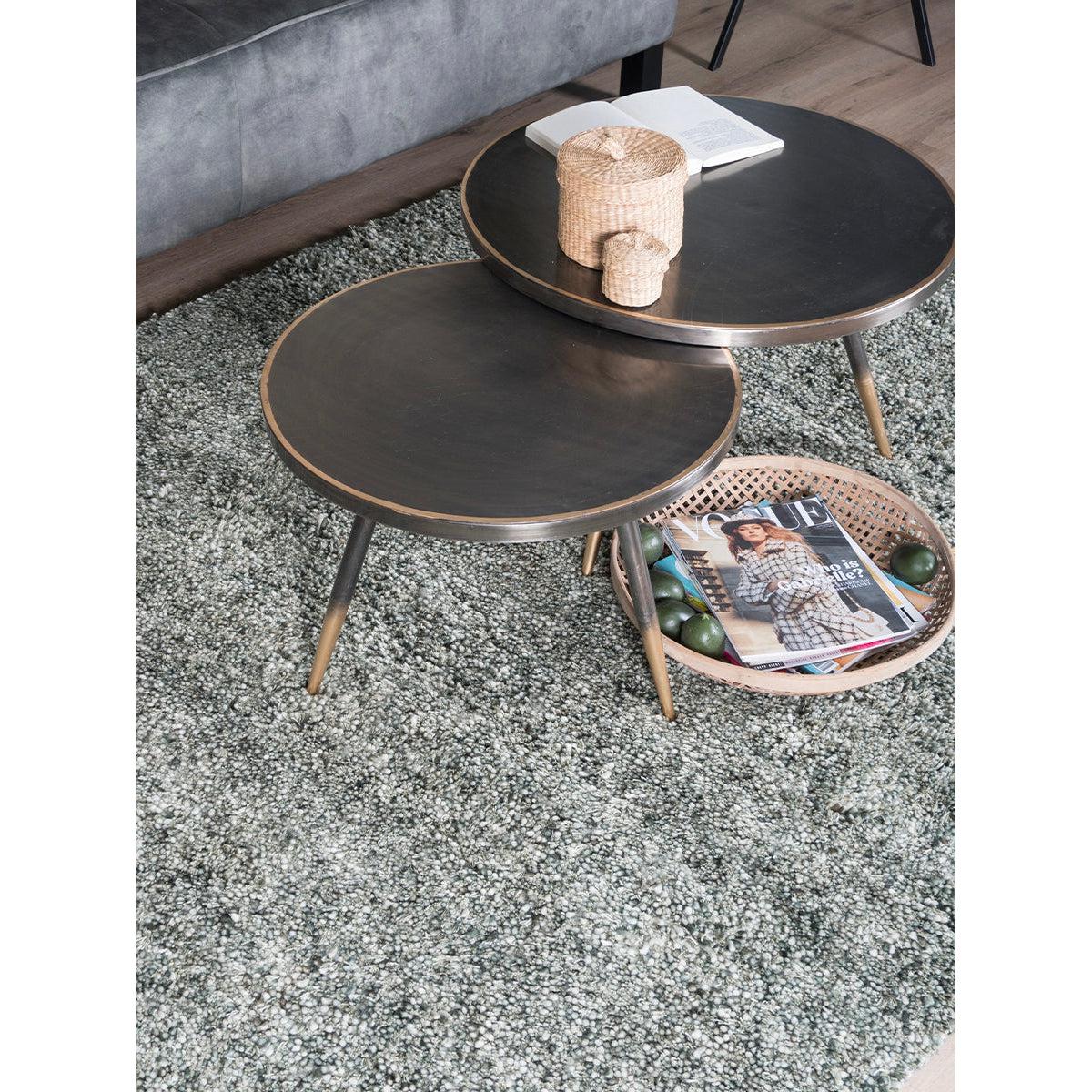 Donkere bijzettafels met rotan mand, tijdschrift Vogue en decoratieve potten op grijs tapijt.