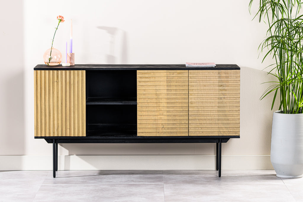 Moderne houten kast met zwart frame, vaas met bloem en kaarsen linksboven, naast een groene plant.