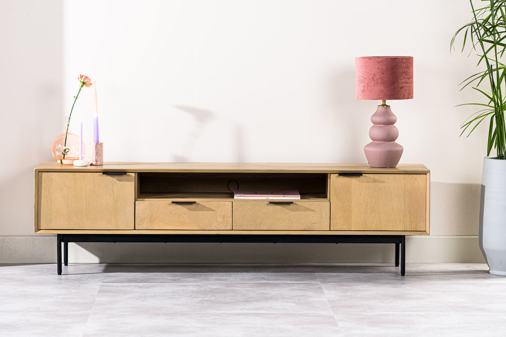 Houten dressoir met roze lamp, gekleurde kaarsen en een plant naast een witte muur in een moderne kamer.
