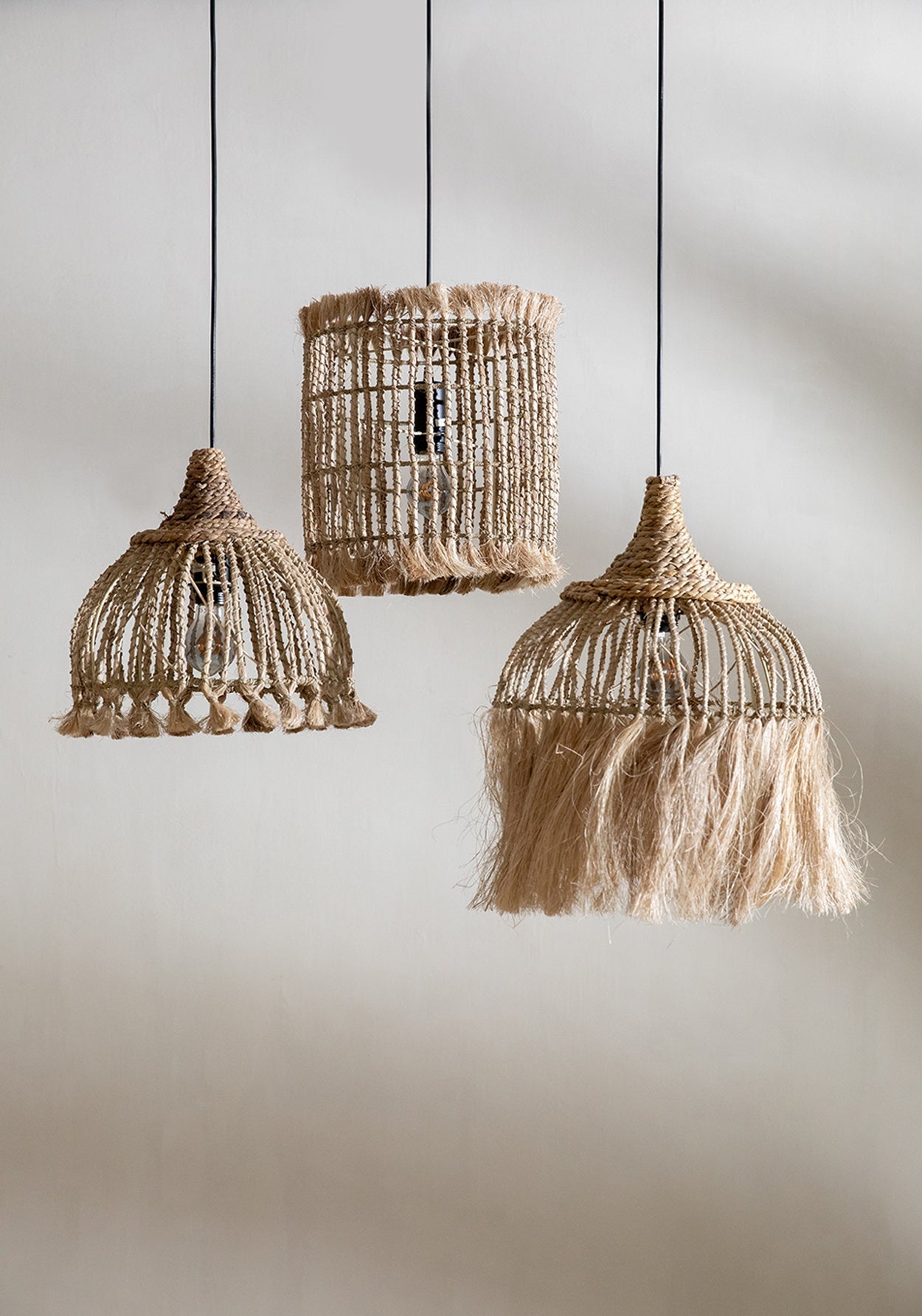 Drie hanglampen van natuurlijke vezels met unieke, handgemaakte ontwerpen tegen een neutrale achtergrond.