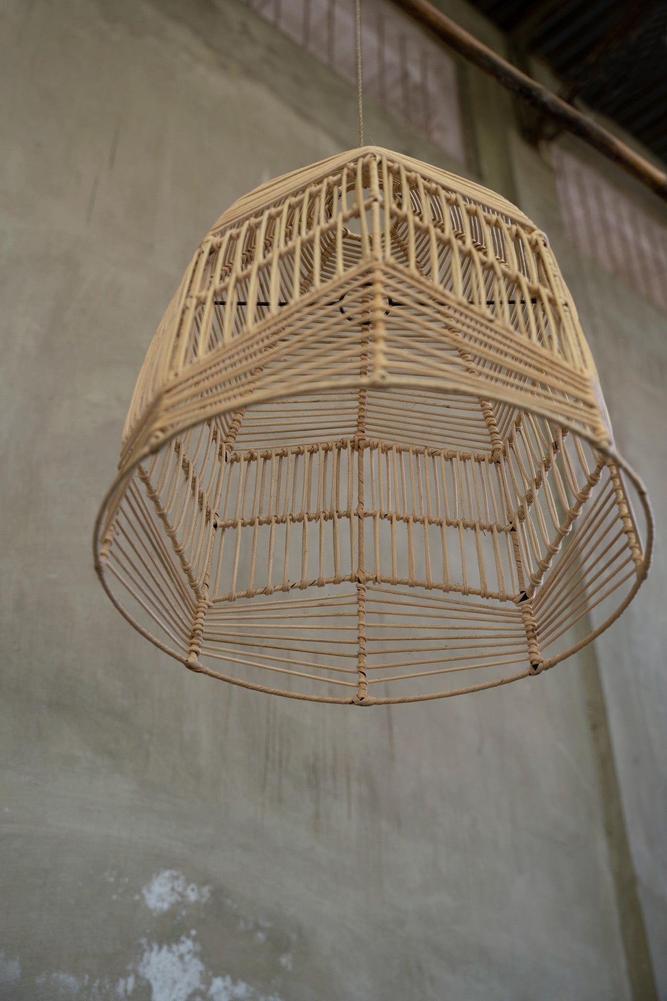 Rotan hanglamp in geometrisch ontwerp hangt aan een ruwe betonnen plafond, straalt rustieke charme uit.