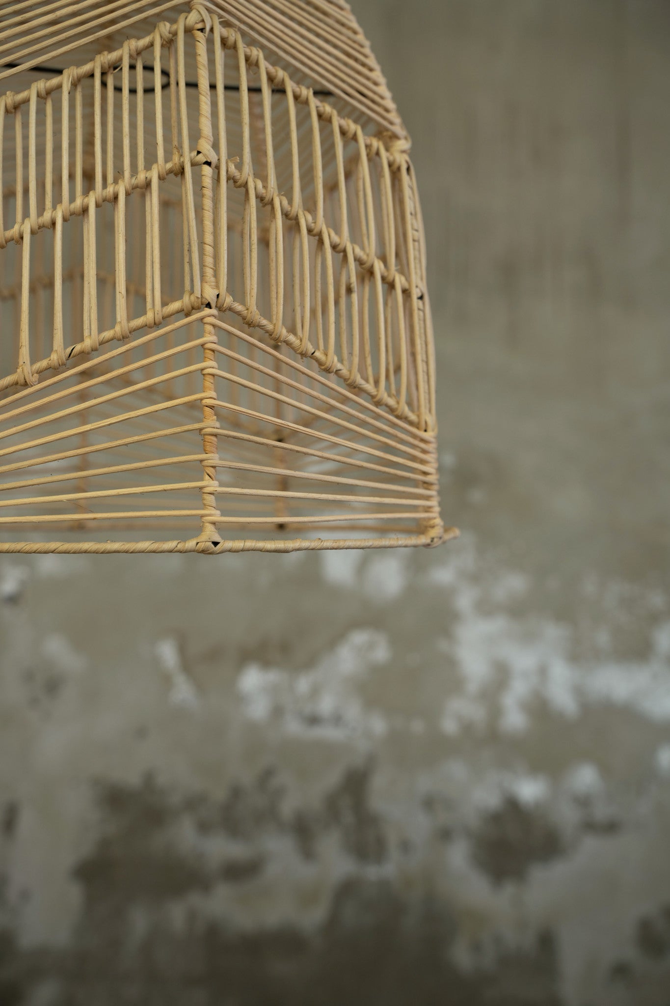 Rieten lampenkap in een moderne, minimalistische stijl tegen een verweerde, grijze betonnen muur.