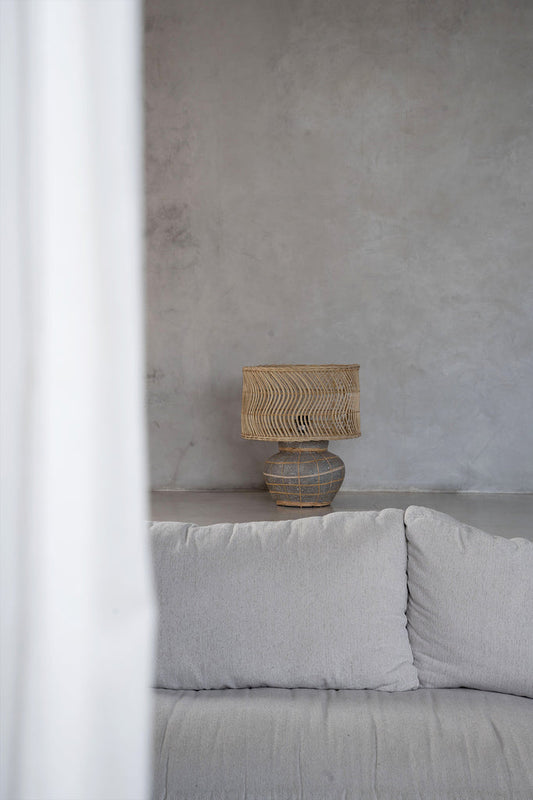 Grijze bank voor betonnen muur met moderne rotan lamp; kalme en minimalistische inrichting.