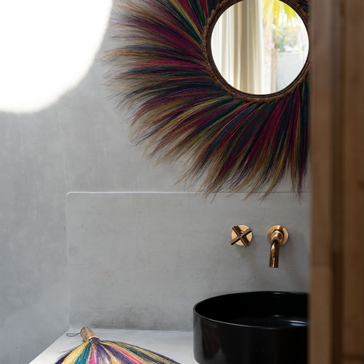 Rond kleurrijk versierde spiegel en gouden kraan boven zwarte wastafel in moderne, minimalistische badkamer.