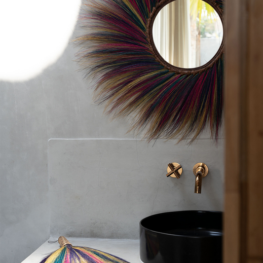 Rond kleurrijk versierde spiegel en gouden kraan boven zwarte wastafel in moderne, minimalistische badkamer.