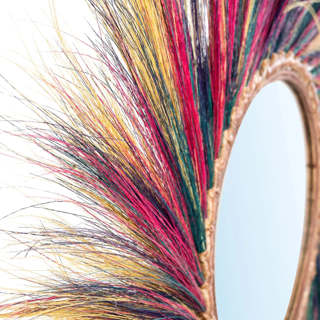 Decoratieve ronde spiegel omlijst met kleurrijke gedroogde grasstelen in roze, geel en blauw tinten.