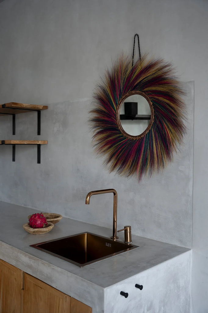 Bruine keuken met gouden kraan, kleurrijke ronde spiegel, en rode pitahaya op betonnen aanrecht.