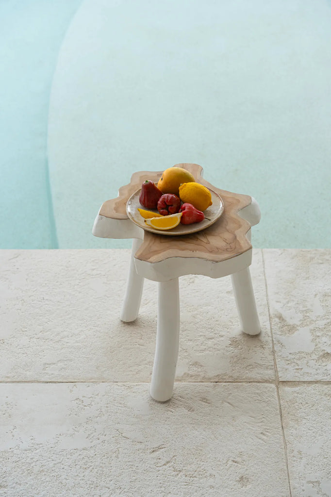 Fruitplate op houten kruk naast zwembad, met citroenen, waxappels en een serene, zonnige sfeer.
