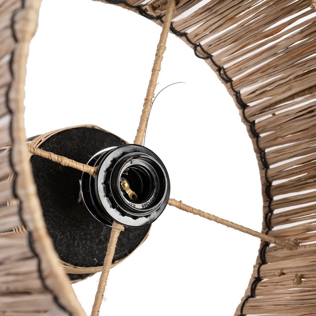 Rieten lampenkap met zichtbare zwarte fitting, gespannen door houten stokken tegen witte achtergrond.