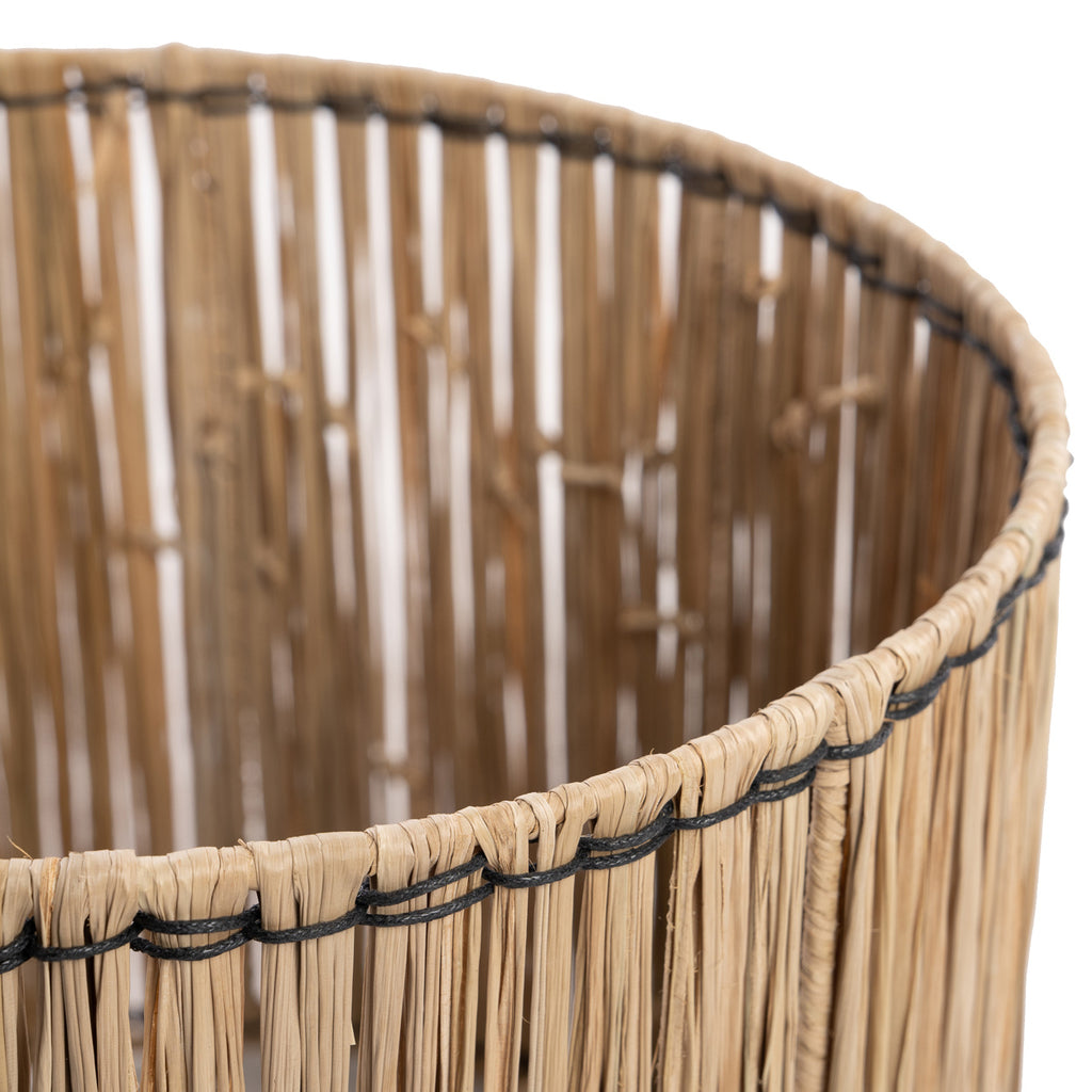 Close-up van een ronde, handgeweven rieten mand met natuurlijke tinten en zwarte draadaccenten.