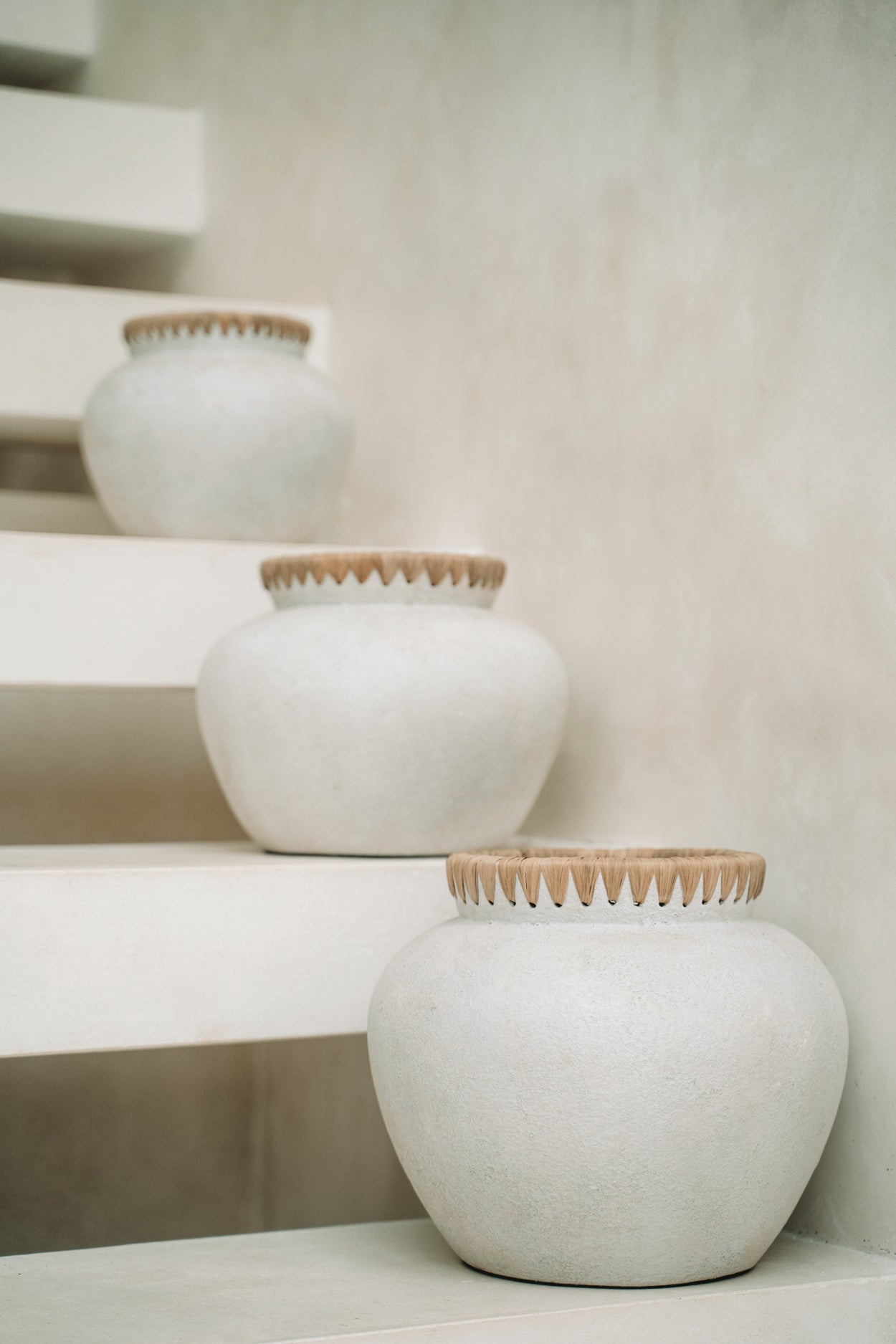 Drie witte keramische vazen met houten rand op minimalistische, beige trap.