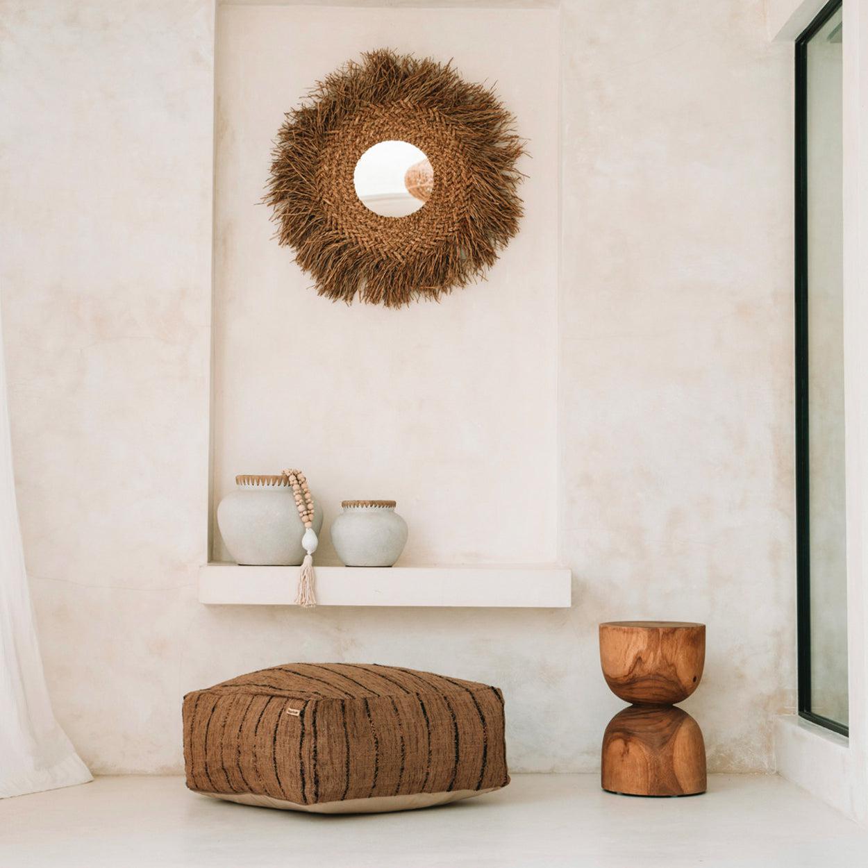 Minimalistisch interieur met natuurlijke tinten, potten op een plank, een stro spiegel en een houten poef.