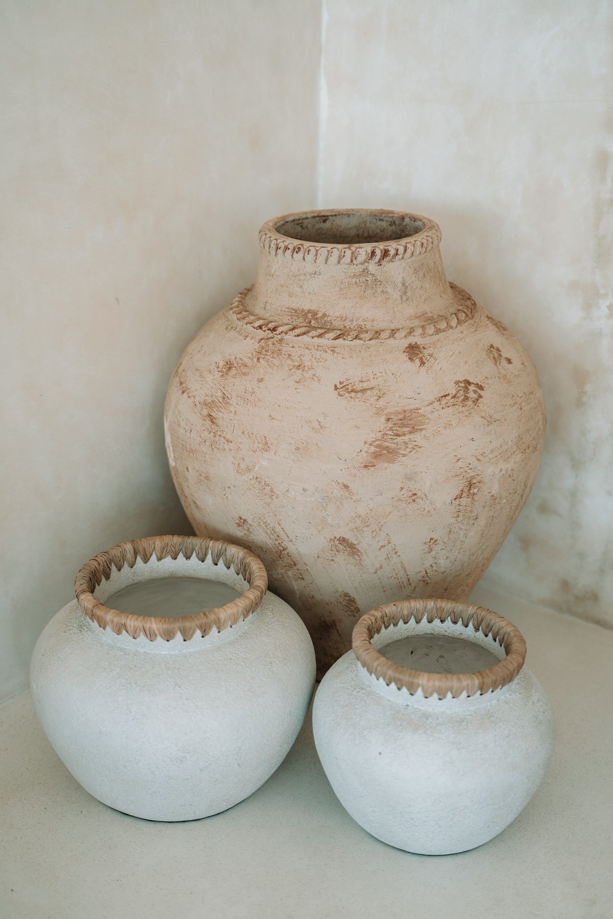 Drie rustieke vazen, twee wit met gevlochten rand en één grotere beige vaas met decoratieve textuur.