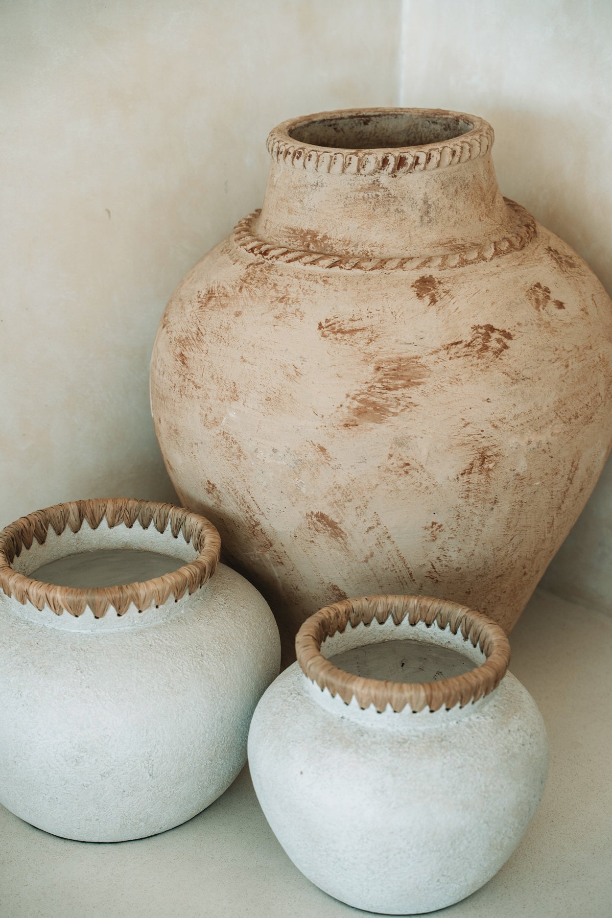 Drie rustieke potten met textuur, twee witte met gevlochten randen, één grote zandkleurige pot.