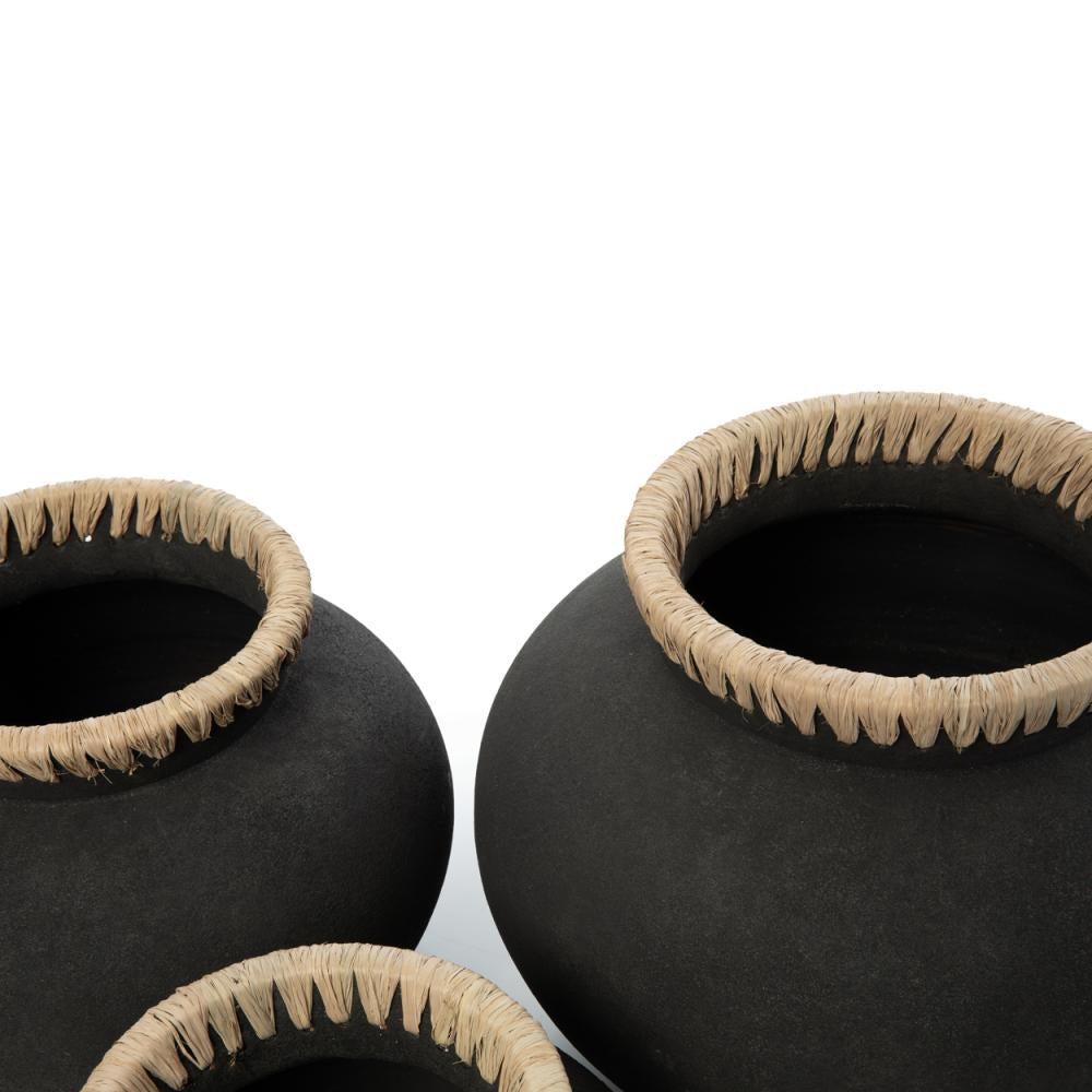 Zwarte keramische potten met beige gevlochten mandenranden tegen een strakke witte achtergrond.