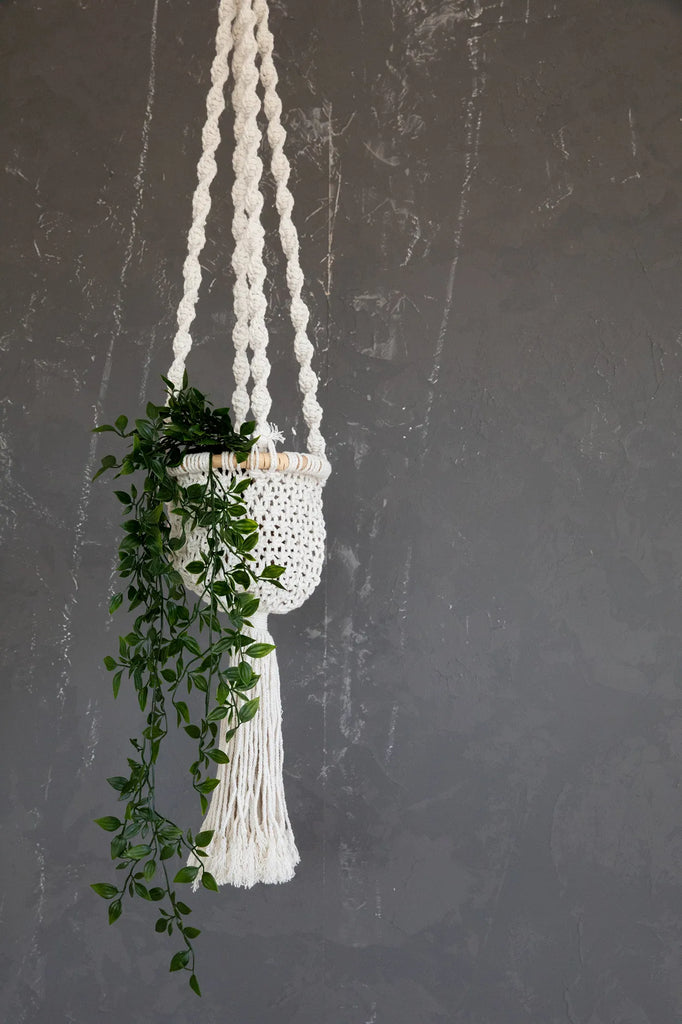 Macramé plantenhanger met groene klimop tegen grijze muur, geeft een bohemian en natuurlijke uitstraling.