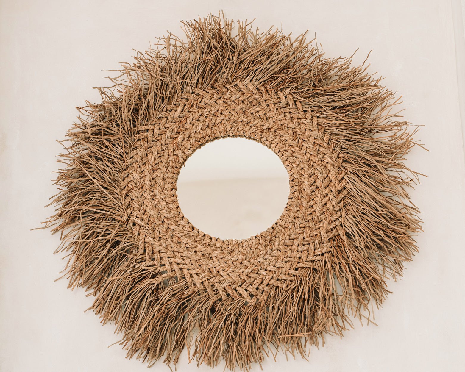 Rond spiegel met een frame van gevlochten stro, geeft een natuurlijke en rustieke uitstraling aan de muur.