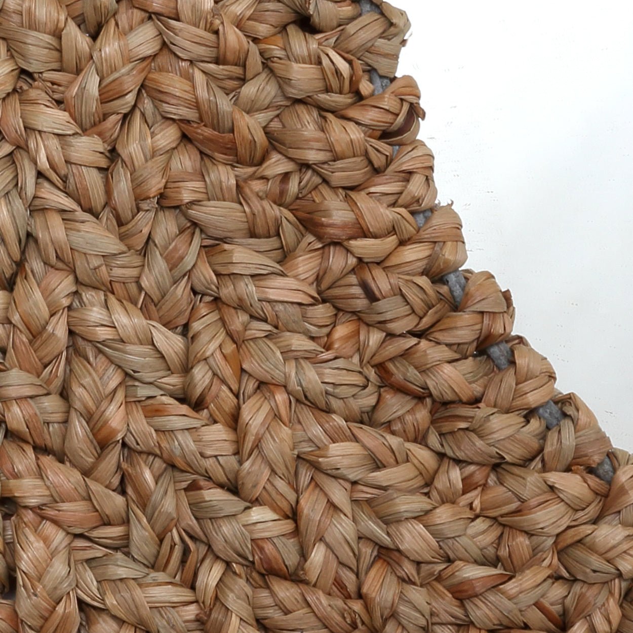 Geverfde rand van een mand met dikke, gevlochten, lichtbruine jute strengen tegen een witte achtergrond.