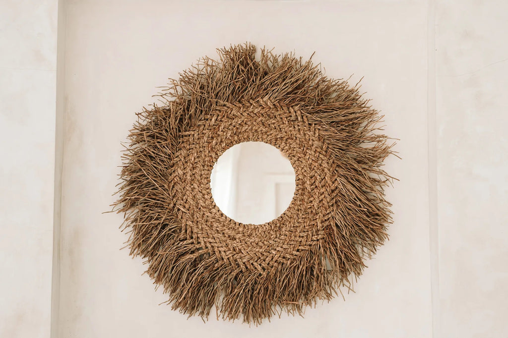 Ronde spiegel met gevlochten rotan frame en speelse strostructuur tegen een lichte muur.
