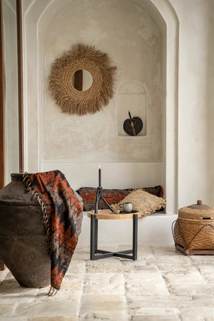 Stijlvol interieur met rieten spiegel, rustieke decoraties, kaars op tafel, en warme, aardse tinten.